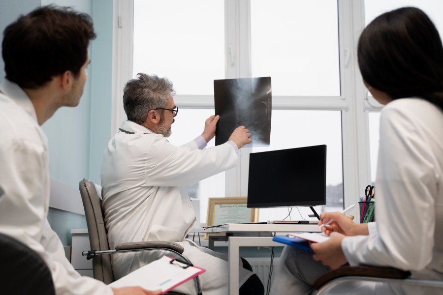 Three doctors in white coats reviewing an X-ray in a medical office.